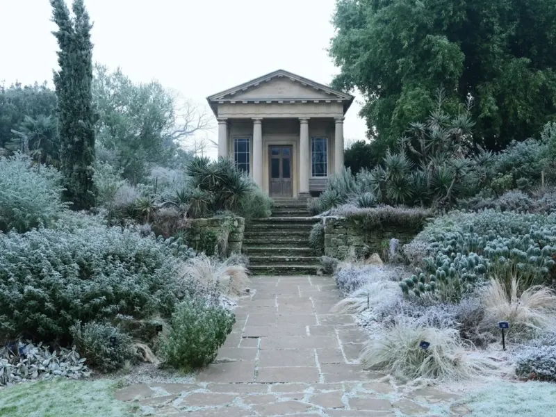 Jardin couvert de givre au petit matin, allée menant à un pavillon