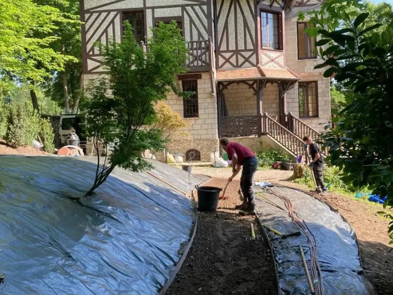 Deux jardiniers plantent un talus couvert de toile de paillage devant une maison à colombages