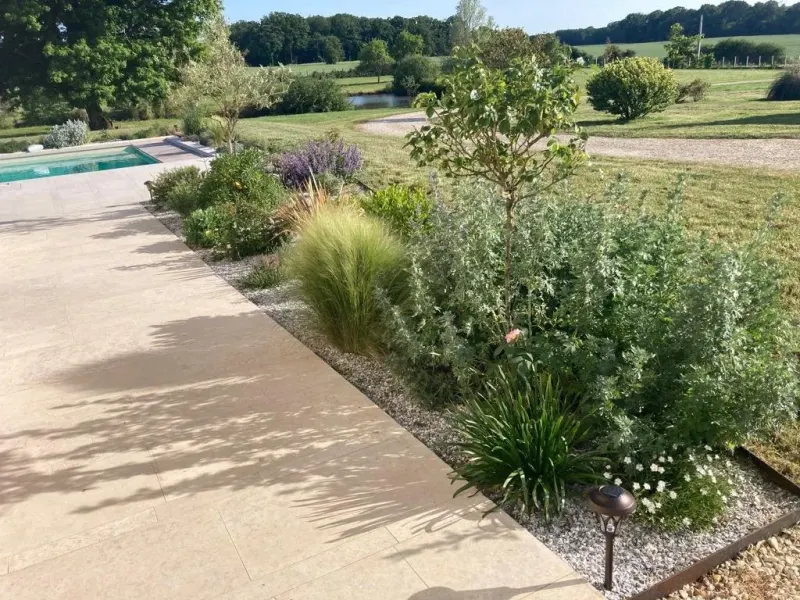 Mixed-border de vivaces, graminées et arbustes fleuris longeant une terrasse de pierre et une piscine, ouverte sur la campagne